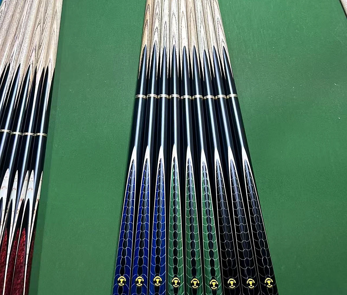 Row of SNOOKERCUE 3/4 jointed snooker cues with hand-laid dragon-scale butts, lined up on the baize